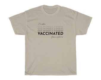 May include: A beige t-shirt with black text that reads "I've been vaccinated" and "You're welcome". The word "vaccinated" is repeated multiple times in a stacked, staggered design.