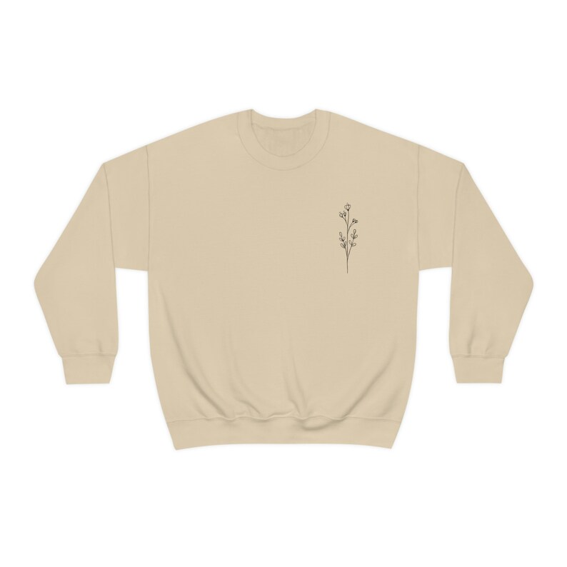 May include: A beige sweatshirt with a small, simple line drawing of a flower on the left chest.