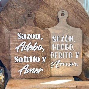 May include: Two wooden cutting boards with the text "Sazon, Adobo, Sofrito y Amor" and "SAZÓN, ADOBO, OFRITO Y Amor" in white lettering.