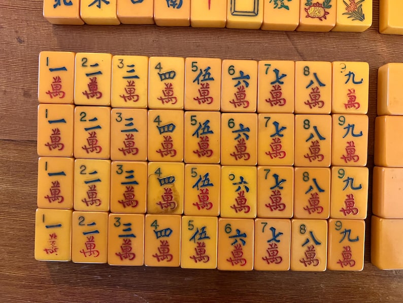 May include: A collection of vintage Mahjong tiles, featuring a warm yellow hue with red Chinese characters. The tiles are arranged in rows, showcasing various numbers and symbols, perfect for game enthusiasts.