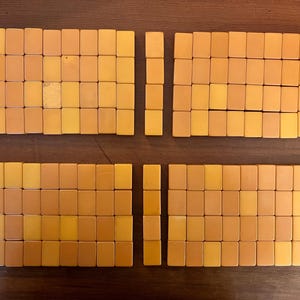 May include: Overhead view of a collection of vintage Mahjong tiles arranged on a wooden surface. The tiles are rectangular, with a warm, yellow-orange hue. The tiles are organized into four groups, with two columns of tiles separated by a small gap.