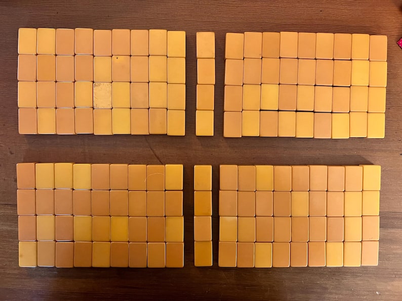 May include: Overhead view of a collection of vintage Mahjong tiles arranged on a wooden surface. The tiles are rectangular, with a warm, yellow-orange hue. The tiles are organized into four groups, with two columns of tiles separated by a small gap.