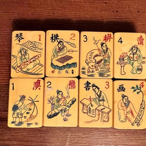 K&ouml;nnte beinhalten: Acht Vintage-Mahjong-Steine in Elfenbeinfarbe mit schwarzen und farbigen Illustrationen von Figuren und Szenen. Jede Kachel hat eine Nummer von 1 bis 4 und chinesische Schriftzeichen. Die Kacheln sind auf einer Holzoberfl&auml;che angeordnet.