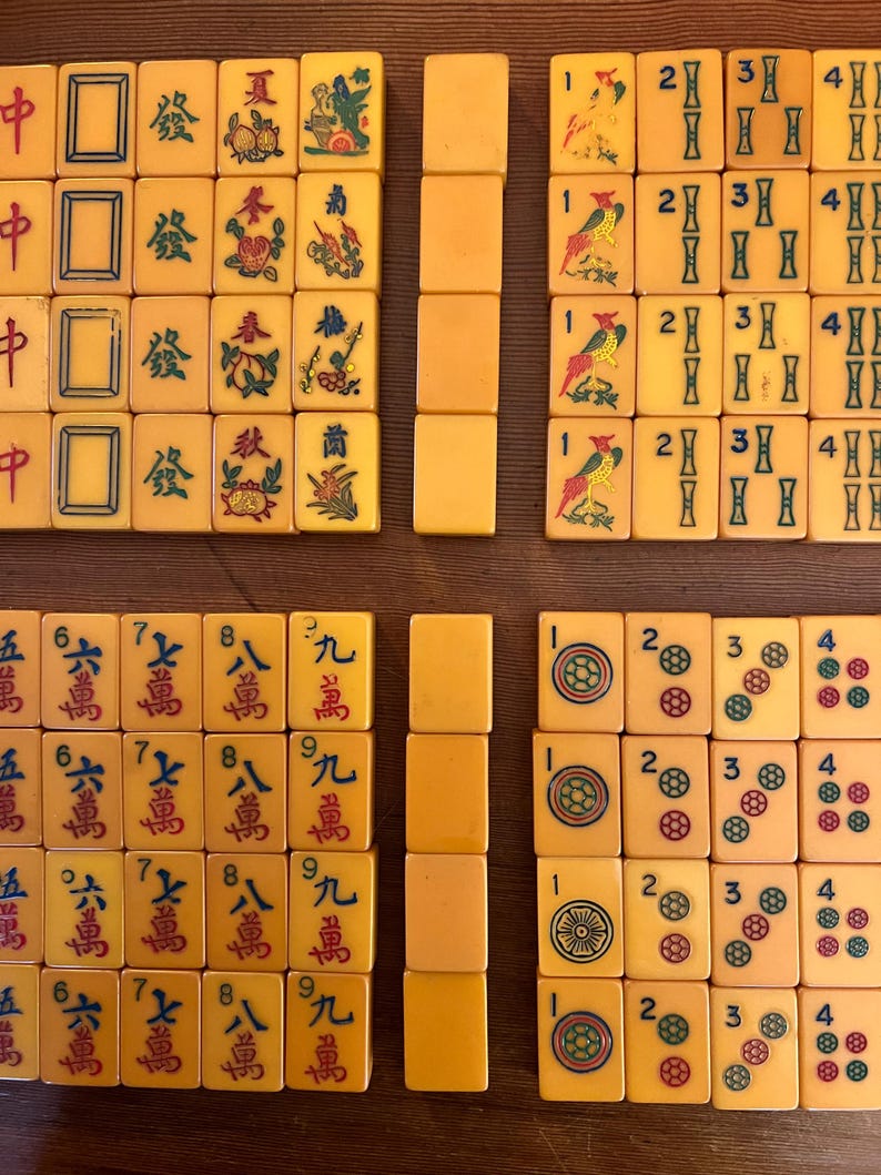 May include: A collection of vintage Mahjong tiles, featuring ivory-colored tiles with red, green, and blue symbols and characters. The tiles are arranged in several groups, showcasing various suits and numbers.