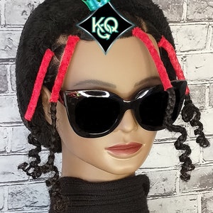 May include: A black mannequin head with curly black hair styled with red hair ties. The mannequin is wearing black sunglasses and a black turtleneck sweater.