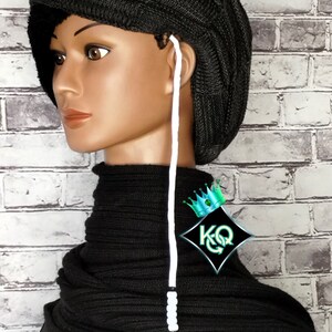 May include: Black knitted beanie with a white string attached. The beanie has a unique shape and is folded down in the front. The string has a small white bead at the end.