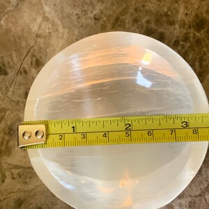 May include: A round, white selenite bowl with a translucent appearance. A yellow measuring tape is placed across the bowl, showing a diameter of approximately 7 inches.