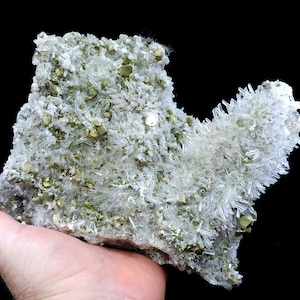 May include: A cluster of clear quartz crystals with a golden brown mineral, possibly pyrite, embedded in the matrix. The crystals are long and slender, with a pointed tip. The matrix is a light brown color.