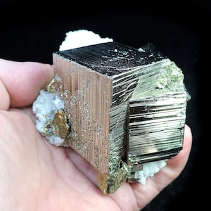 May include: A large, metallic, silver-coloured pyrite crystal with a cubic shape. The crystal has a striated surface and is partially covered in white calcite crystals.