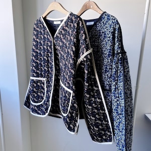 May include: Two jackets hanging on a rack. One is navy blue with a paisley pattern and white trim. The other is navy blue with a floral pattern. Both jackets have a V-neck design.