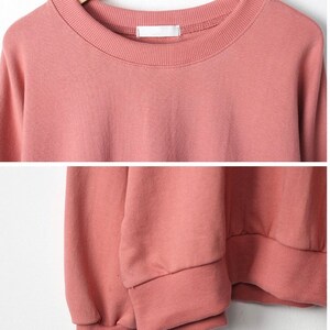 May include: A soft, pink sweatshirt with long sleeves and a crew neck. The sweatshirt has a ribbed neckline and cuffs.
