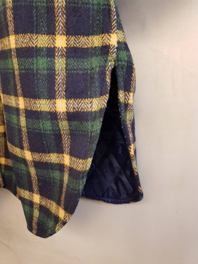 May include: A garment featuring a dark navy blue, forest green, and bright yellow plaid pattern. The outer layer has a textured, wool-like appearance, while the interior lining is a solid dark navy blue fabric with a quilted diamond stitch pattern.