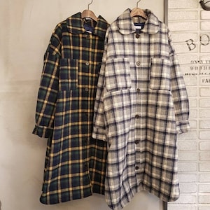 May include: Two long plaid coats hanging on wooden hangers. One coat is navy, green, and yellow plaid. The other is gray, white, and navy plaid. Both coats have a rounded collar, button closures, and pockets.