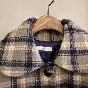 May include: A gray coat featuring a plaid pattern in navy blue, white, and yellow lines. The coat has a rounded collar and a dark blue quilted interior lining. A white label with the text Bona is sewn into the inner neckline of the garment.