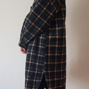 May include: A long-sleeved, knee-length shirt jacket featuring a dark navy blue, forest green, and mustard yellow plaid pattern. The garment has a classic collar, a button-down front, long sleeves with cuffs, and a curved hem with side slits.