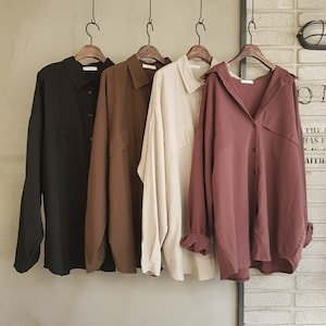 Peut inclure: Quatre chemises à manches longues suspendues à des cintres. Les chemises sont noires, brunes, beiges et bordeaux.