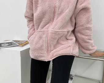 May include: A pink fuzzy zip-up jacket with a high collar and two pockets.