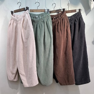 May include: Four pairs of corduroy pants hanging on hangers. The pants are in different colors: light pink, green, brown, and black.