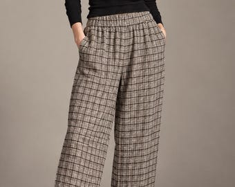 May include: A pair of wide-leg trousers featuring a brown, black, and white plaid pattern, an elasticized waistband, and side pockets, paired with a long-sleeved black crew-neck top and black slip-on loafers.