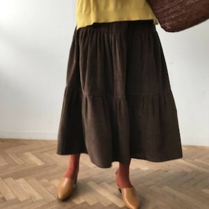 May include: A brown corduroy tiered skirt with a long length. The skirt has a relaxed fit and is made of a soft, comfortable fabric.