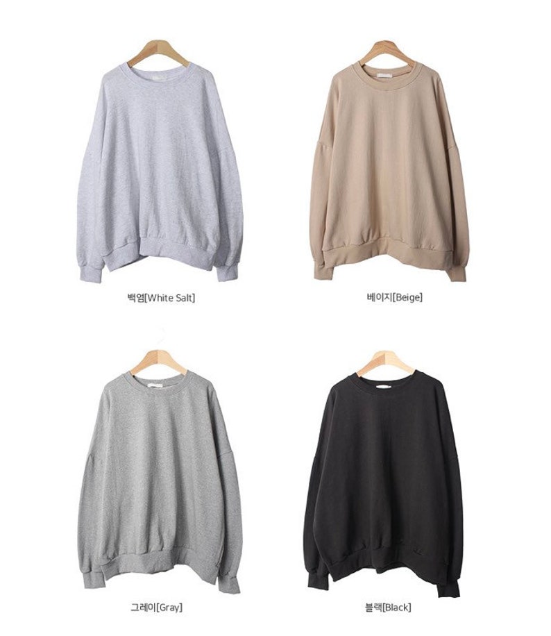 May include: Four sweatshirts in different colours: white salt, beige, grey, and black. The sweatshirts have a relaxed fit and a round neckline.