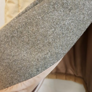 Puede incluir: Primer plano del interior de una chaqueta acolchada beige. El forro es de tela gris claro con un forro liso y sedoso debajo.