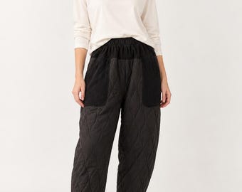 May include: A long-sleeved cream-colored crewneck shirt paired with black quilted trousers featuring an elastic waistband, two large front patch pockets, and a tapered leg silhouette that ends just above the ankle, worn with black slip-on shoes.
