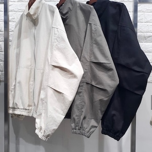 May include: Three jackets hanging on a rack. The jackets are made of a lightweight fabric and have a zipper closure. The jackets are in beige, gray, and black.