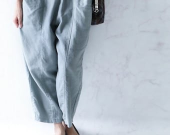 May include: Light blue, loose-fitting trousers with an elastic waistband, two large front patch pockets, and vertical seam detailing down the front of each leg. The pants are paired with a plain white long-sleeved top and light gray ballet flats.