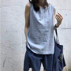Könnte beinhalten: Ein hellblaues ärmelloses Oberteil mit Rundhalsausschnitt, kombiniert mit einer dunkelblauen Shorts und einer dunkelblauen Tragetasche mit dem weißen Schriftzug Maison Kitsune Paris. Das Set besteht aus einem locker sitzenden Oberteil.