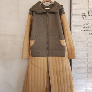 Puede incluir: Una chaqueta larga con capucha de color marr&oacute;n y beige con cierre de cremallera. La chaqueta tiene una secci&oacute;n inferior acolchada y un bolsillo de parche a cada lado.