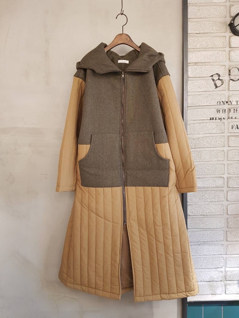 Puede incluir: Una chaqueta larga con capucha de color marr&oacute;n y beige con cierre de cremallera. La chaqueta tiene una secci&oacute;n inferior acolchada y un bolsillo de parche a cada lado.