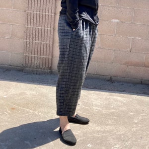 May include: Grey and black checked trousers with a wide leg and a relaxed fit. The trousers are cropped and have a slight flare at the bottom.