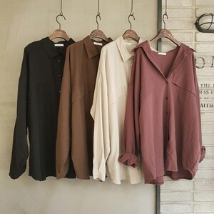 Könnte beinhalten: Vier langärmlige Button-Down-Hemden in Schwarz, Braun, Beige und Mauve, hängen an Holzbügeln. Die Hemden haben eine lockere Passform und werden vor einer neutralen Wand präsentiert. Die Hemden sind aus einem weichen, leichten Stoff gefertigt.