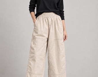 May include: A black long-sleeve crew neck shirt paired with beige wide-leg cropped pants. The pants feature an elasticized waistband, side pockets, and visible stitching details along the front panels. The outfit is completed with black flat shoes.