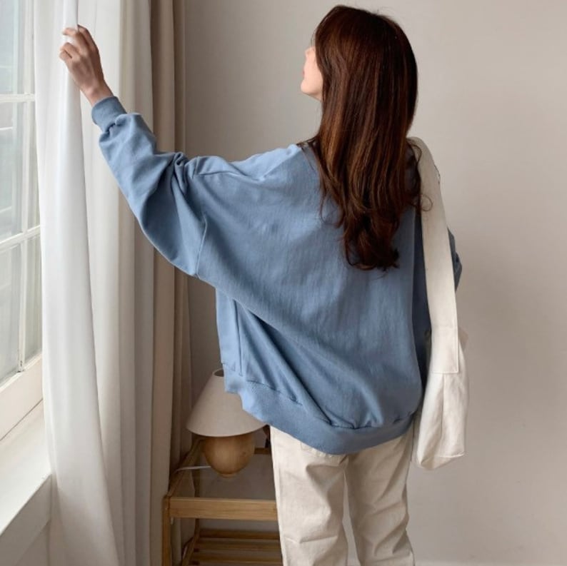 May include: A light blue oversized sweatshirt with long sleeves and a relaxed fit. The sweatshirt is made of a soft, comfortable fabric and has a casual style.