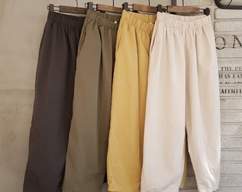May include: Four pairs of wide-leg pants hanging on wooden hangers. The pants are in brown, green, yellow, and white.