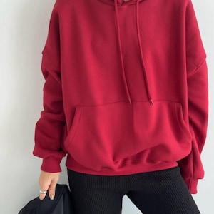 以下が含まれることがあります： ドローストリングフードとカンガルーポケットが付いた、オーバーサイズの赤いフーディーです。