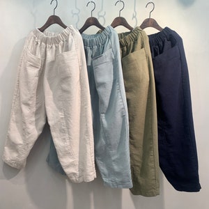 May include: Four pairs of wide-leg pants hanging on hangers. The pants are in different colors: white, light blue, olive green, and navy blue. The pants have a relaxed fit and a drawstring waist.