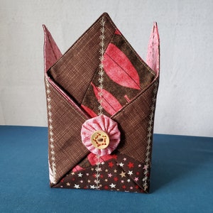 May include: A brown and pink fabric storage box with a star pattern and a pink button. The box is folded into a square shape.