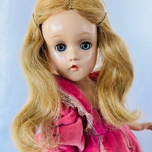 May include: A vintage porcelain doll with blonde hair, blue eyes, and a pink velvet dress with lace trim.