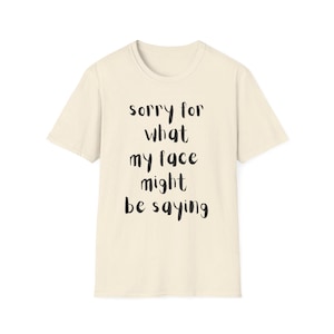以下が含まれることがあります： 「sorry for what my face might be saying」の黒い文字がプリントされたクリーム色のTシャツ。クルーネックと半袖で、カジュアルな普段着に最適です。