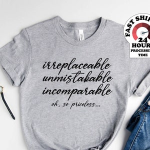 May include: Gray t-shirt with the text "irreplaceable unmistakable incomparable oh, so priceless..." printed on it. The shirt is laid out on a white surface with a pair of blue jeans and white sneakers.