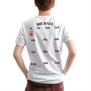 K&ouml;nnte beinhalten: Wei&szlig;es T-Shirt mit schwarzem Text, der "MICHAEL" und die Zahlen von 1. bis 12. lautet. Ein roter Handabdruck ist neben dem Buchstaben "K" zu sehen.