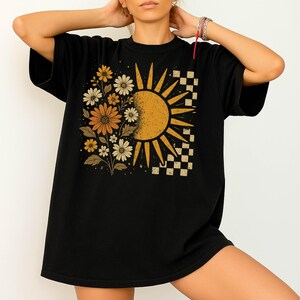 A woman wearing a black t-shirt with a sun and flower design on it.