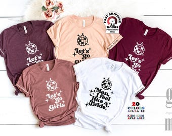 Könnte beinhalten: Fünf kurzärmelige T-Shirts in Kastanienbraun, Pfirsich und Weiß. Jedes Shirt zeigt eine schwarze Grafik einer Discokugel mit Sternakzenten. Vier Shirts tragen den Text "Let's go Girls" und ein weißes Shirt den Text "Man, I feel like a Bride".