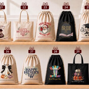 a collection of bags and drawstring bags with various designs and messages, including "Happy Mother's Day", "You Ain't", "Graduate", "Bridal", "Happy Father's Day", and "Happy Birthday".
