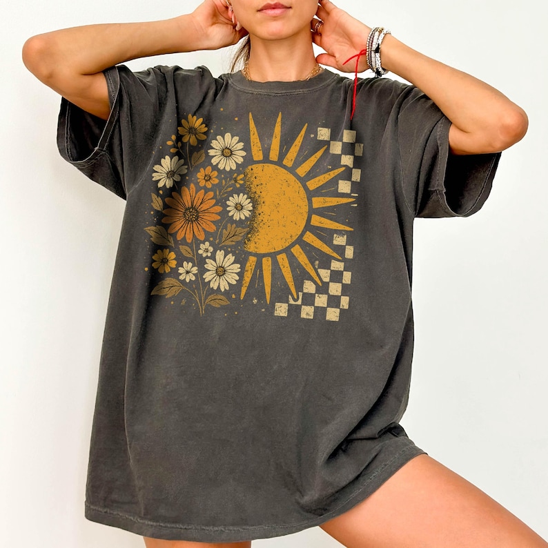 A woman wearing a gray t-shirt with a sun and flower design on it.