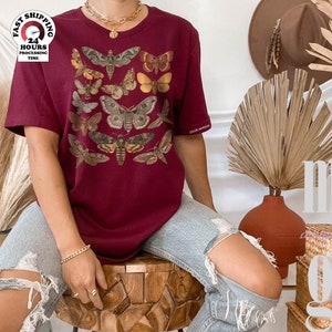 May include: A maroon t-shirt with a vintage illustration of moths and butterflies. The shirt has a relaxed fit and a crew neck.
