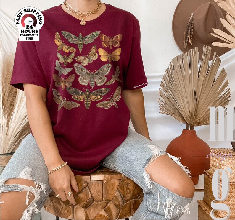 May include: A maroon t-shirt with a vintage illustration of moths and butterflies. The shirt has a relaxed fit and a crew neck.